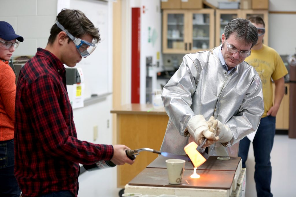 Students work in the lab during Associate Professor Matthew Ray's Chemistry of Materials class An engineering student works on mathematics coursework in Jarvis Hall Thursday, September 28, 2017. Pictured is the class comparing amorphous glass behavior with the crystalline solid behavior observed in the first part of the lab. They prepared batches of soda lime glass and varied the ingredients to change the melt viscosity and color. Glasses of various colors were prepared by adding small amounts of metal oxides to the glass mixture before firing to melt and react all of the ingredients together. The glass mixtures were placed into crucibles and heated overnight to 1150°C (2100°F), then poured onto an iron slab and allowed to cool. To observe fluorescence, the europium and terbium doped samples were illuminated with an ultraviolet lamp (365 nm light) which revealed the bright red and green fluorescence. (UW-Stout Photo by Brett T. Roseman)